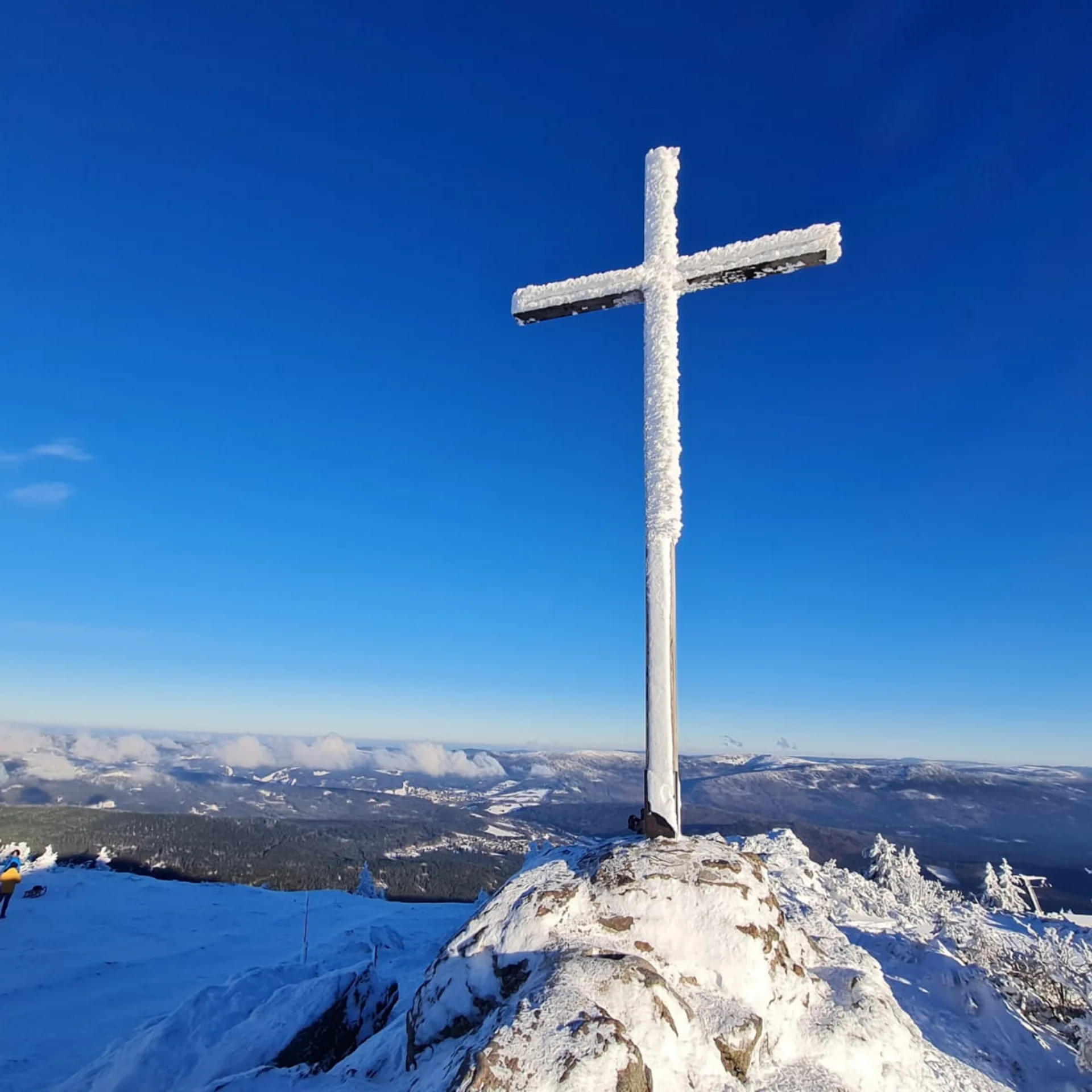 Verschneites Gipfelkreuz auf einem Berg mit klarem blauem Himmel