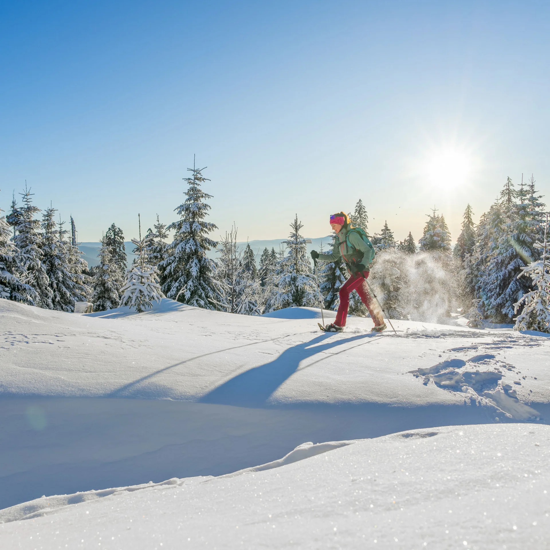 Person beim Schneeschuhwandern in verschneiter Winterlandschaft mit Sonnenlicht