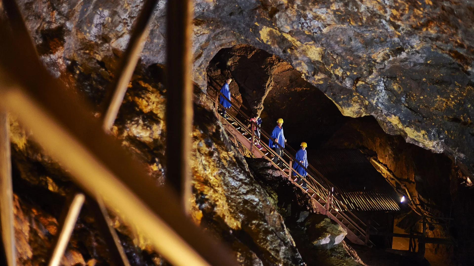 Cubea | Urlaub³ im Bayerischen Wald Besucher in blauen Anzügen und Helmen steigen eine Treppe in einer beleuchteten Höhle hinab