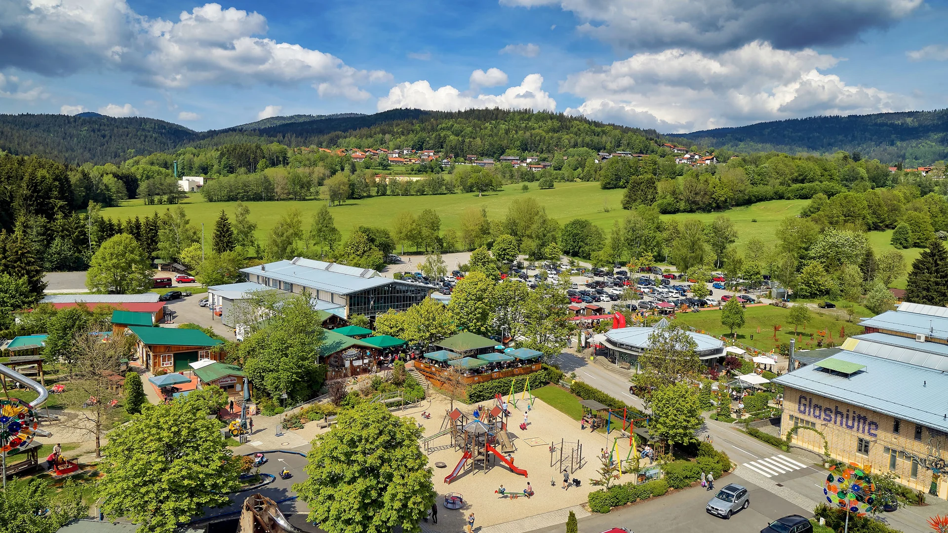 Cubea | Urlaub³ im Bayerischen Wald Luftaufnahme eines Spielplatzes und Parkplatzes in grüner Landschaft mit Bergen im Hintergrund