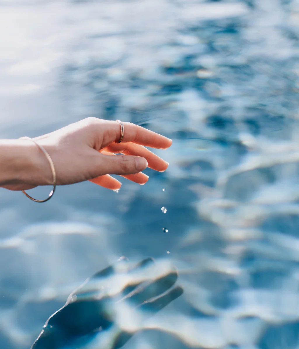 Hand berührt Wasseroberfläche mit fallenden Wassertropfen