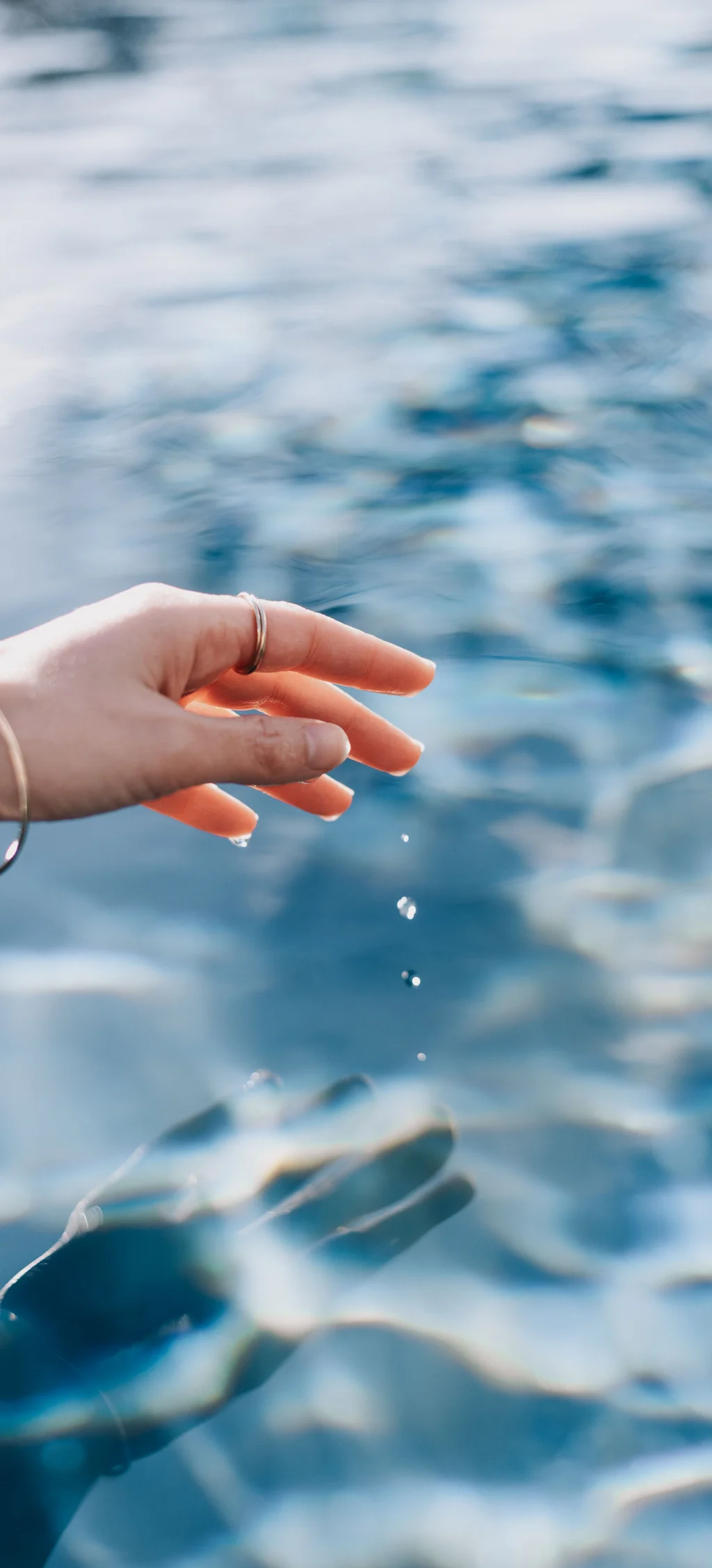 Hand berührt Wasseroberfläche mit fallenden Wassertropfen