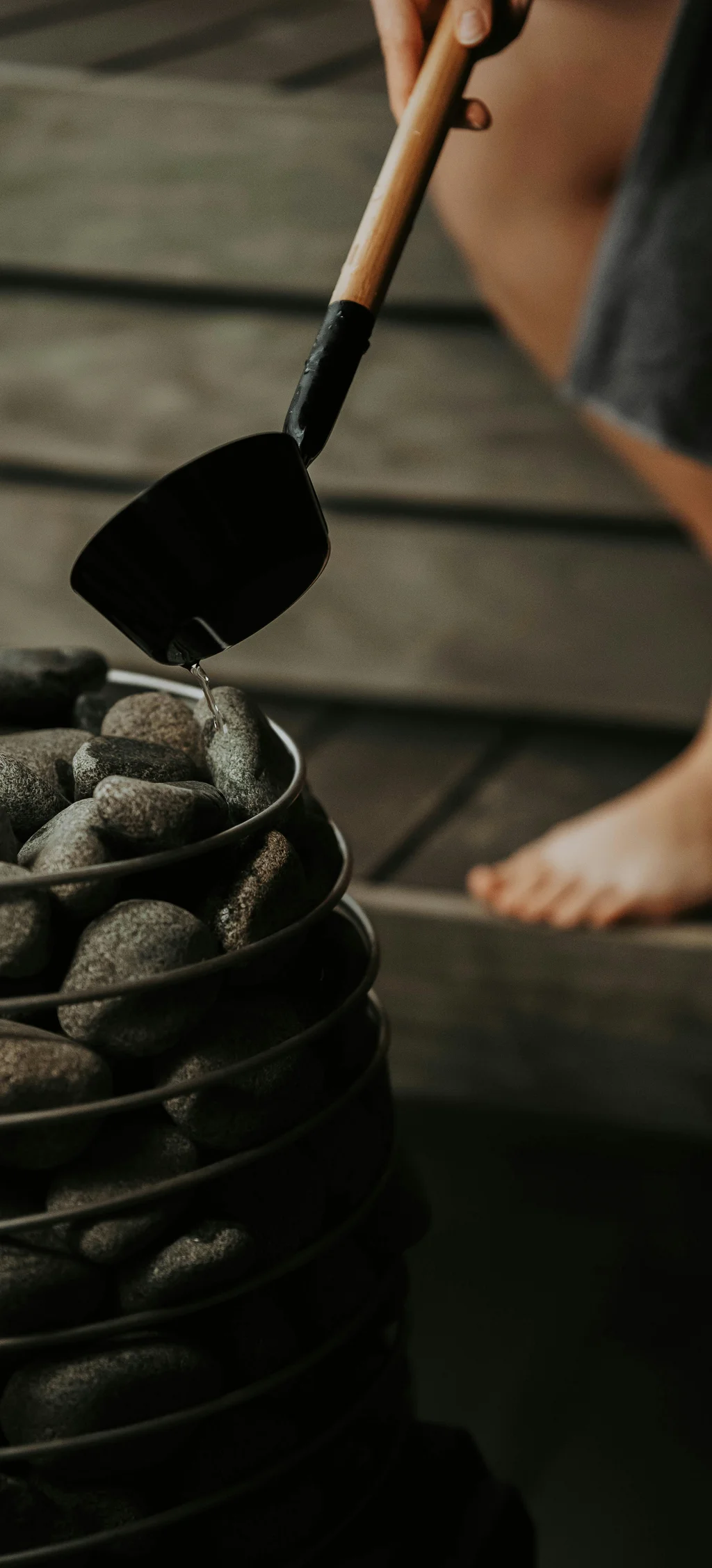 Wasser wird mit einer Kelle auf heiße Steine in einer Sauna gegossen
