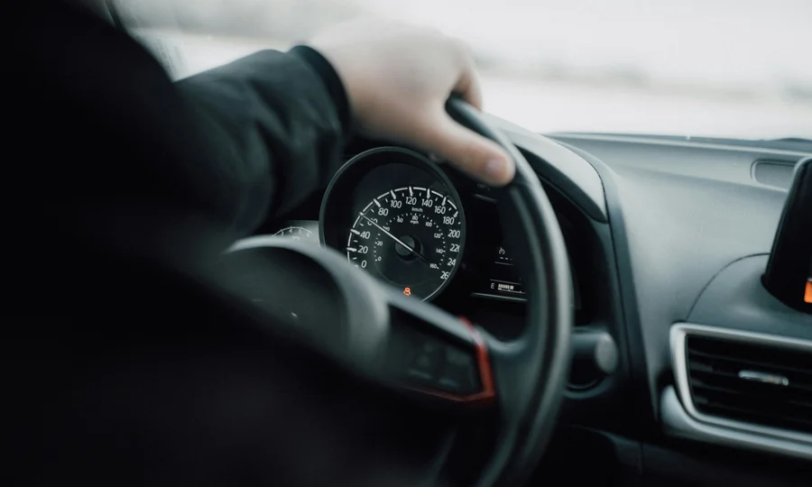 Cubea | Anreise und häufig gestellte Fragen Hand am Lenkrad eines Autos mit sichtbarem Tachometer