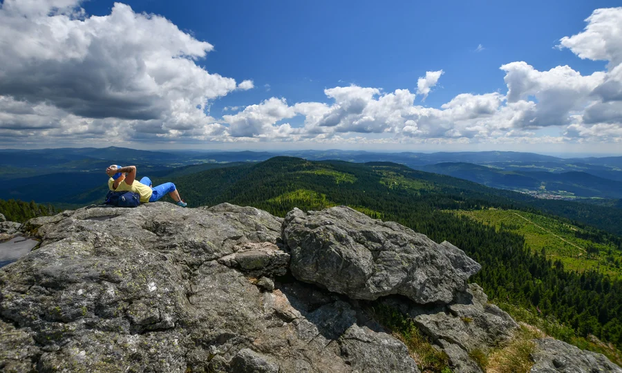 Person entspannt auf Felsen mit Blick auf bewaldete Berge und blauen Himmel