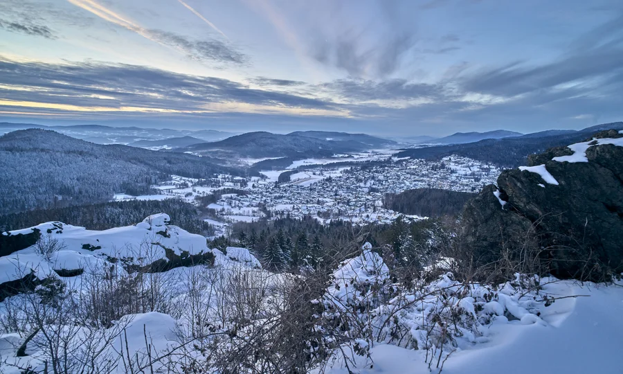 Verschneite Berglandschaft mit Tal und Dorf unter bewölktem Himmel