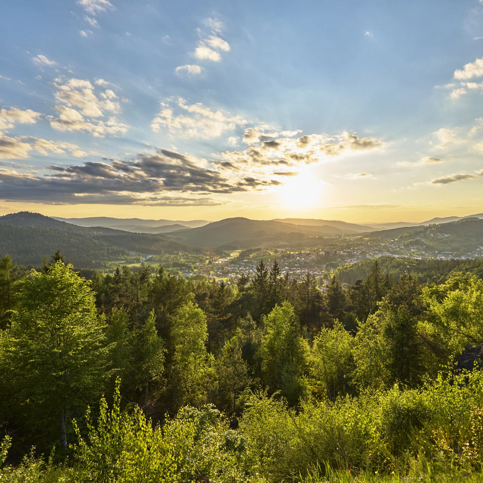 Sonnenuntergang über bewaldeten Hügeln und einem Tal mit Dorf