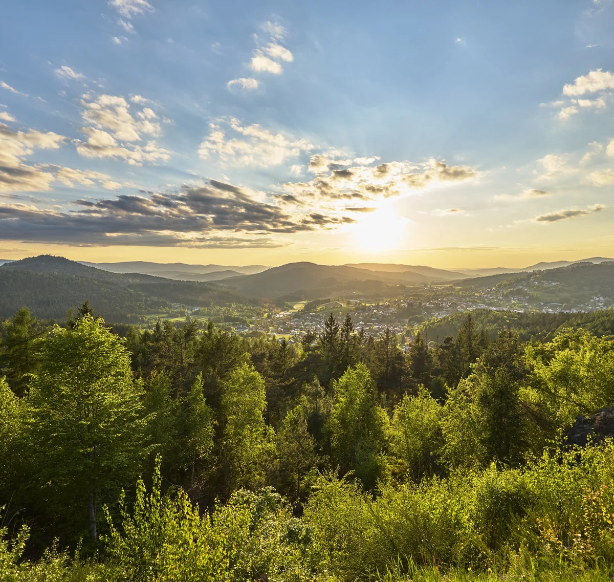 Sonnenuntergang über bewaldeten Hügeln und einem Tal mit Dorf