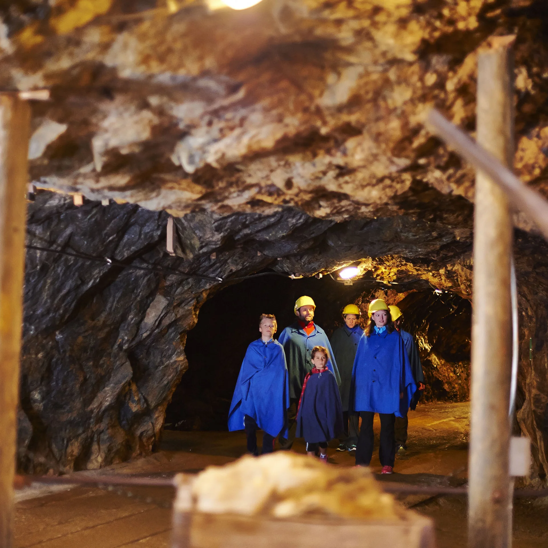 Touristen mit Schutzhelmen und Umhängen in einem beleuchteten Bergwerksstollen