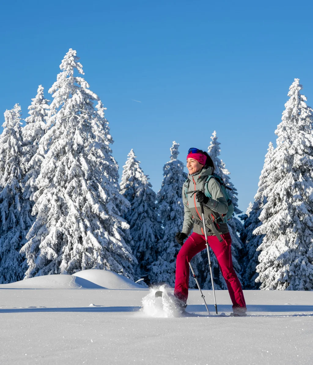 Frau beim Schneeschuhwandern im verschneiten Wald bei klarem Himmel