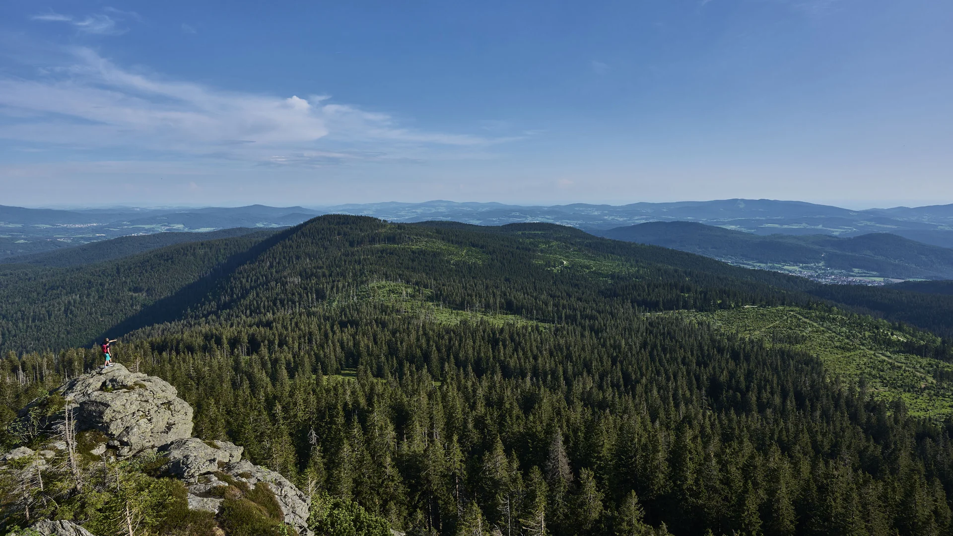 Cubea | Urlaub³ im Bayerischen Wald Wanderer auf Felsen mit Blick auf bewaldete Berge unter blauem Himmel