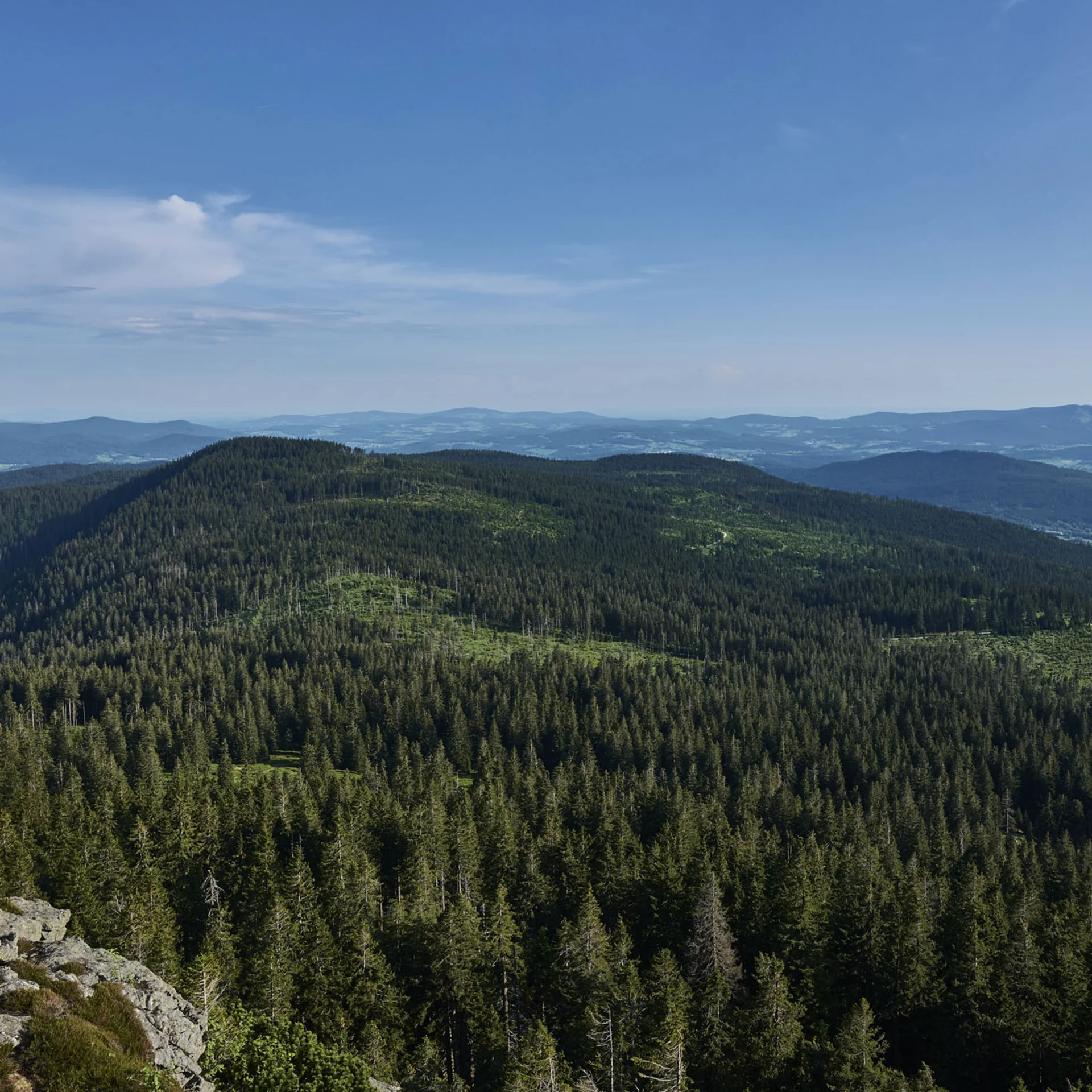 Wanderer auf Felsen mit Blick auf bewaldete Berge unter blauem Himmel