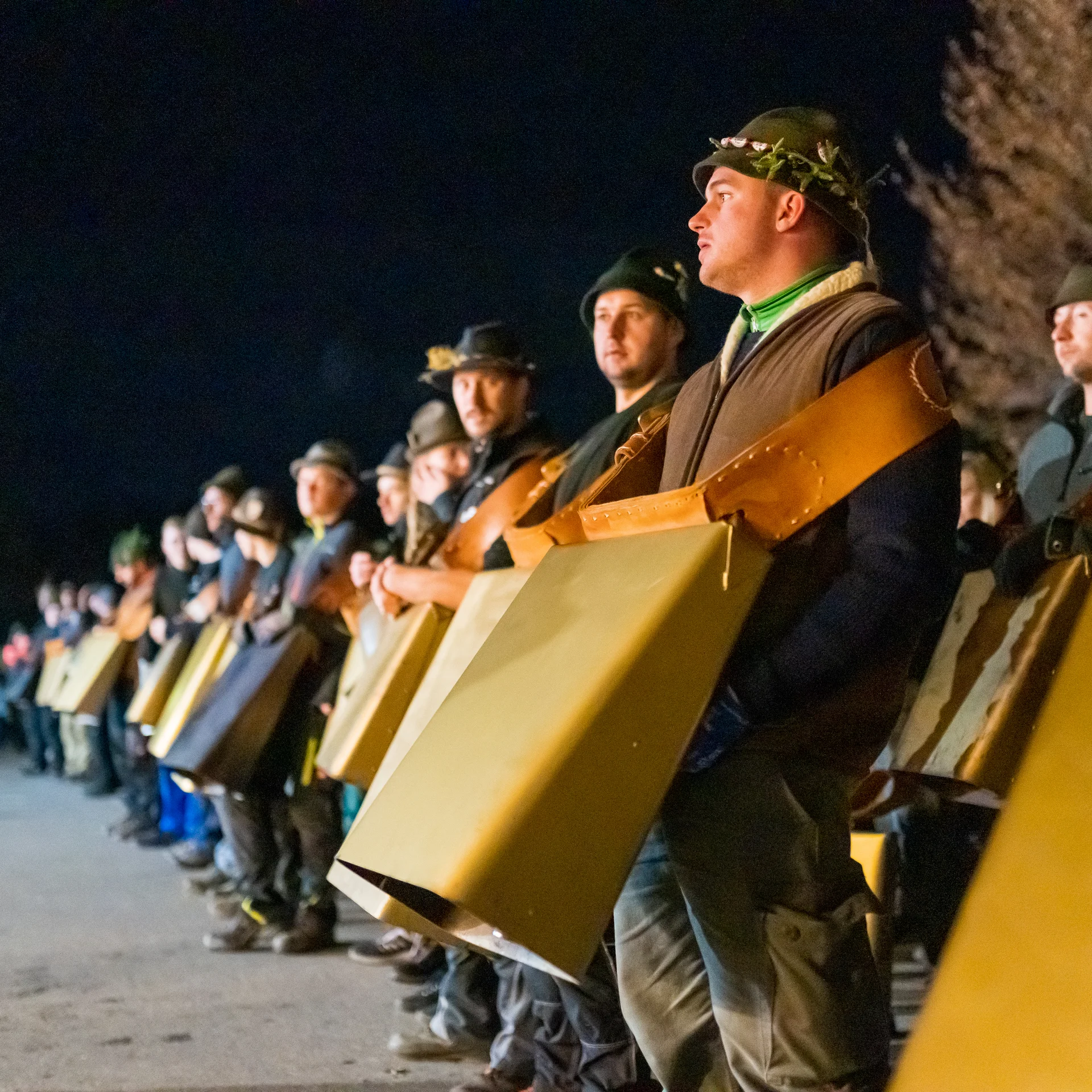 Männer in traditioneller Kleidung mit großen Kuhglocken bei Nacht