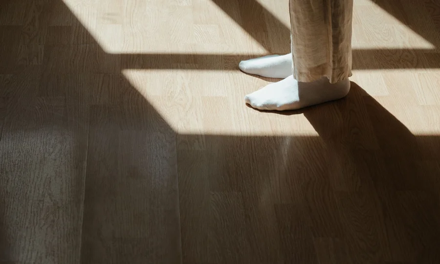 Füße in weißen Socken stehen auf Holzboden im Sonnenlicht
