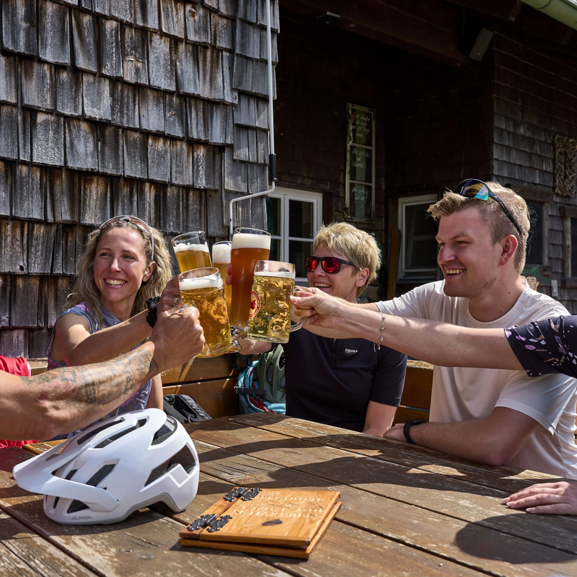 Gruppe von fünf Personen stößt mit Biergläsern an einem Holztisch an