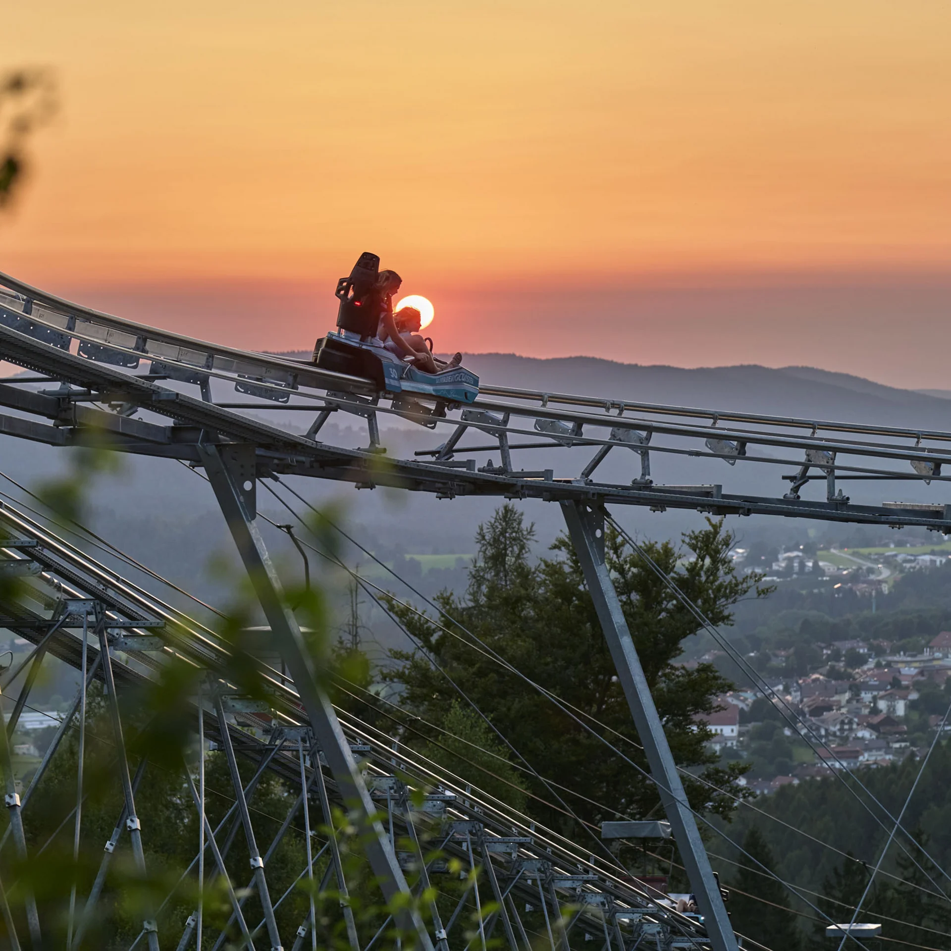 Zwei Personen fahren mit einer Sommerrodelbahn bei Sonnenuntergang