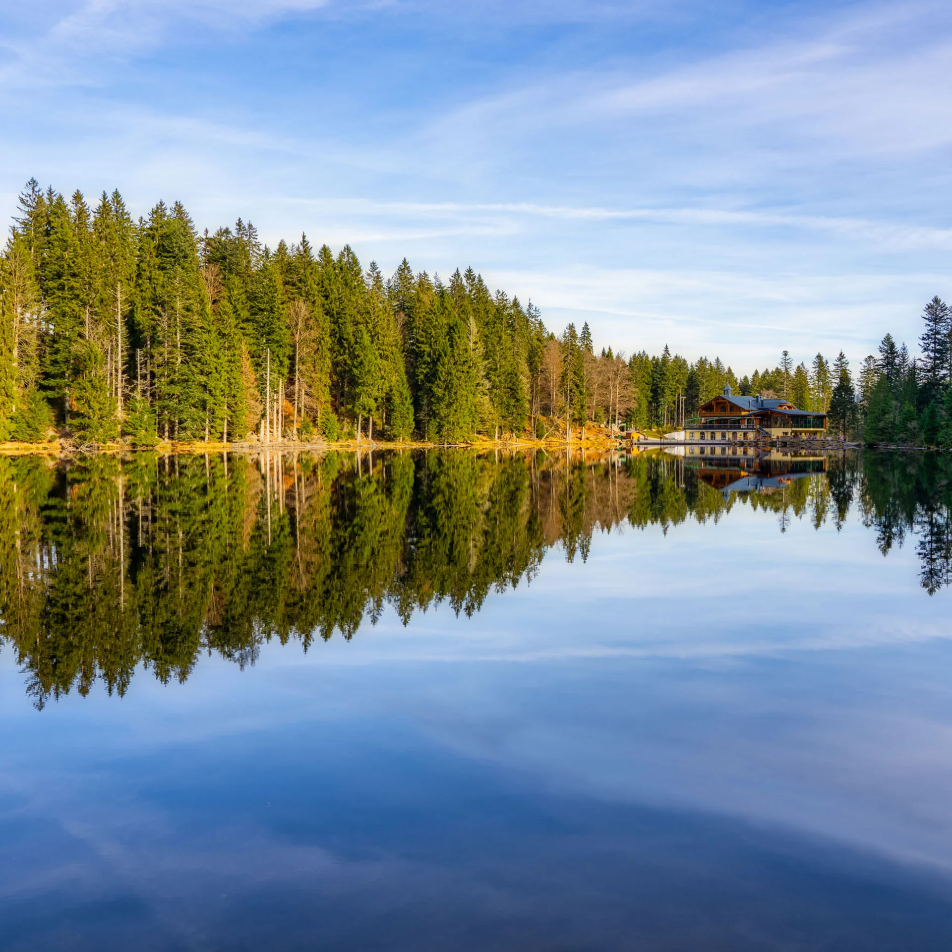 Haus am ruhigen See mit Spiegelung von Bäumen und blauem Himmel
