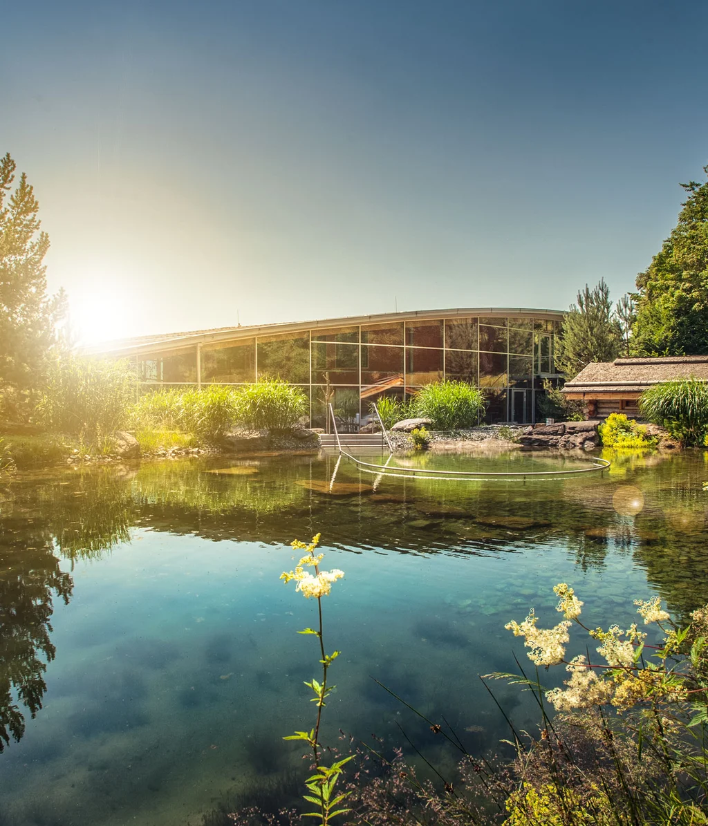 Sonniger Teich mit Spiegelung und modernem Gebäude im Hintergrund