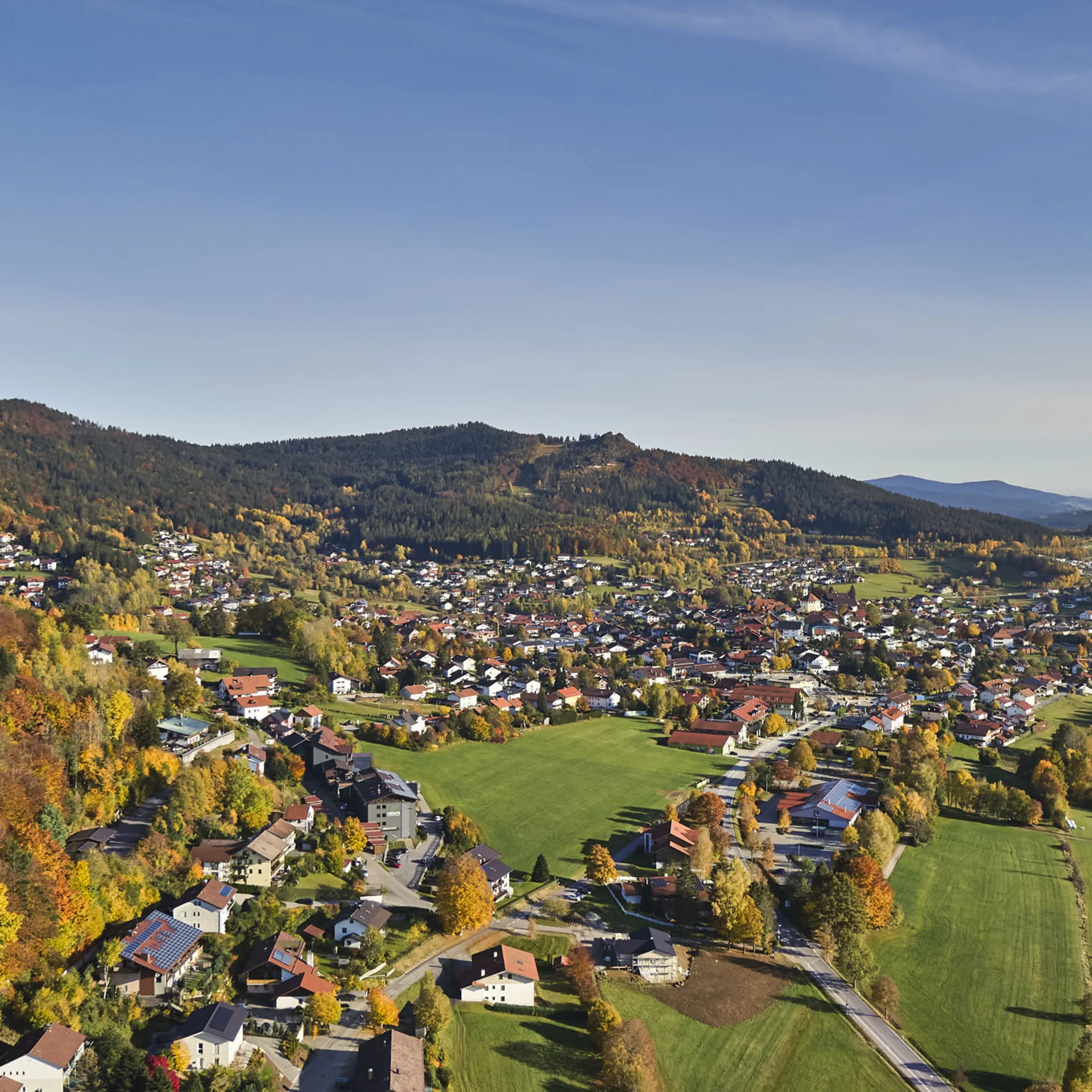 Luftaufnahme eines Dorfes mit bunten Herbstbäumen und grünen Feldern