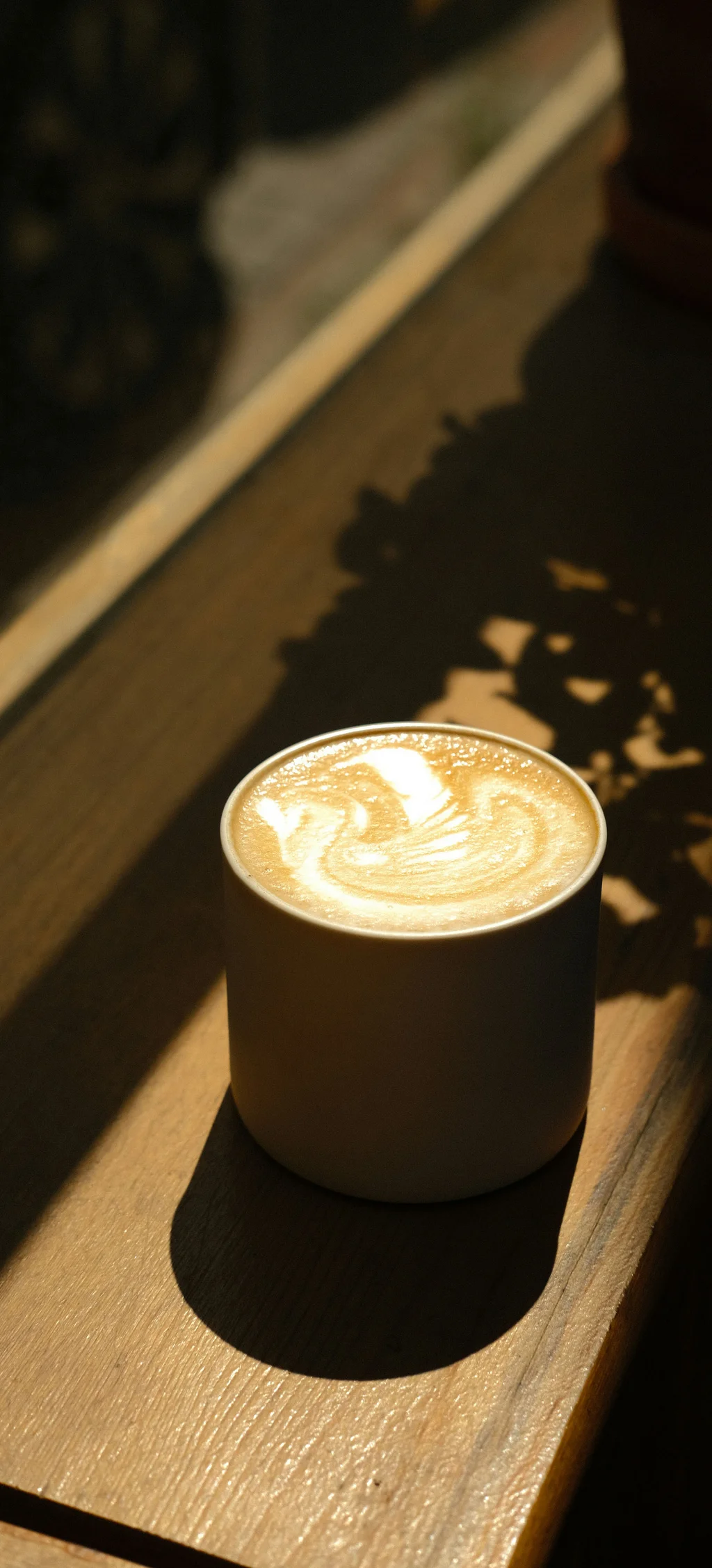 Tasse Kaffee mit Milchschaum und Latte Art auf Holzfensterbank im Sonnenlicht